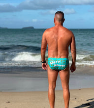 Load image into Gallery viewer, Man wearing blue Sustainable Mens Swim Briefs by Salty Johnson AU standing on beach facing ocean