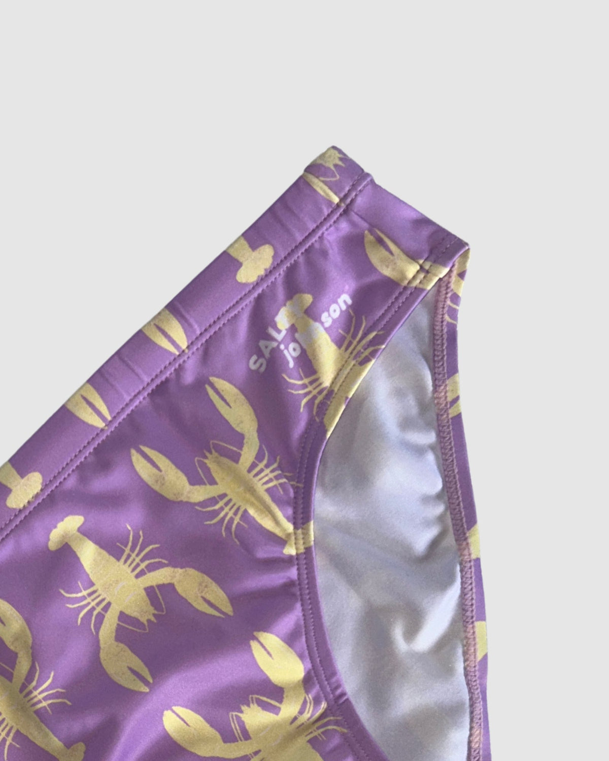 Waistband and front lining detail of Salty Johnson Yabbies men's swim briefs in purple, yellow.