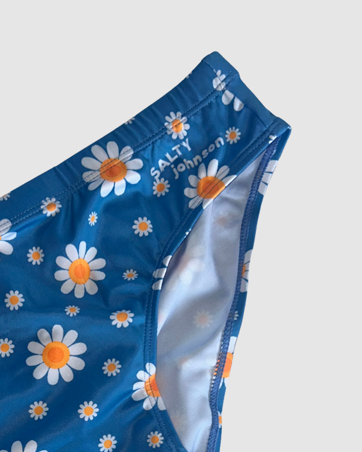 Waistband and front lining detail of Salty Johnson Oopsie Daisy men's swim briefs in blue, white, orange.