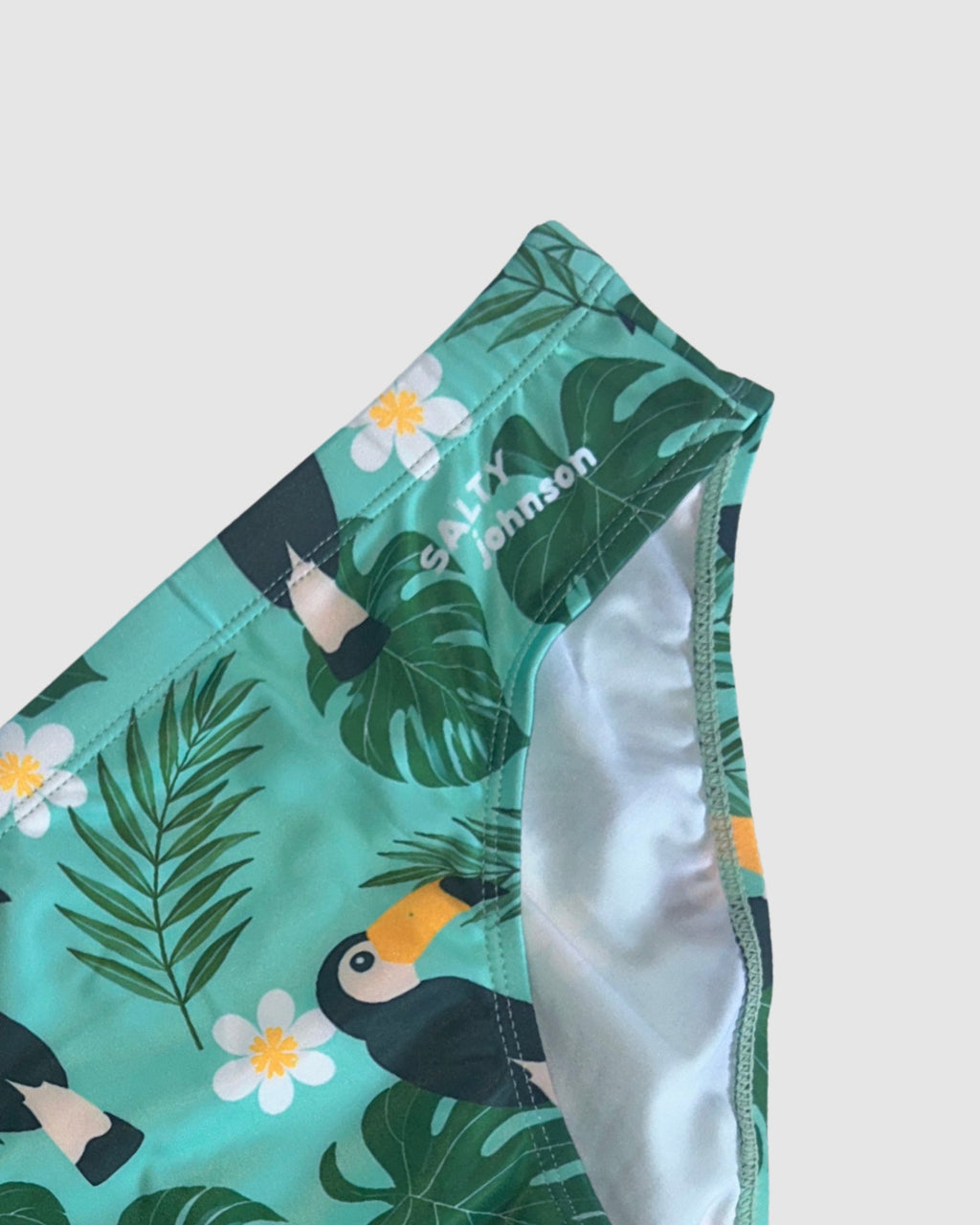Waistband and front lining detail of Salty Johnson Toucan Tango men's swim briefs in green, black, yellow.