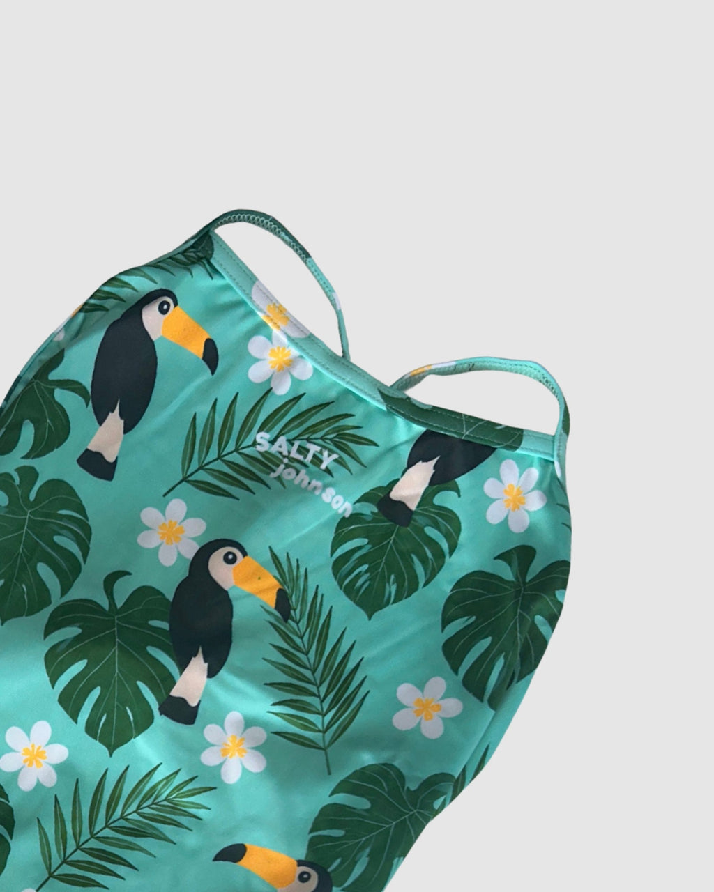 Neckline and print detail of Toucan Tango women's thin strap one-piece swimsuit, toucans and tropical leaves on green.