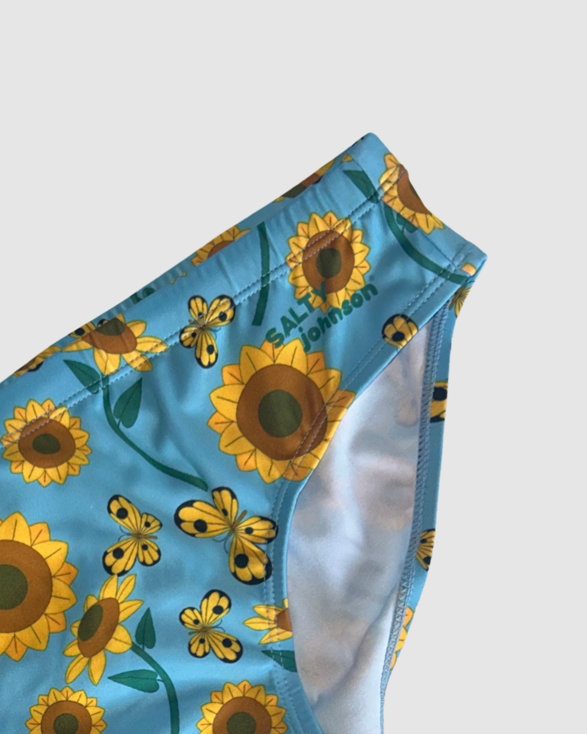 Waistband and front lining detail of Salty Johnson Sunny Side Up men's swim briefs in blue, yellow, green.