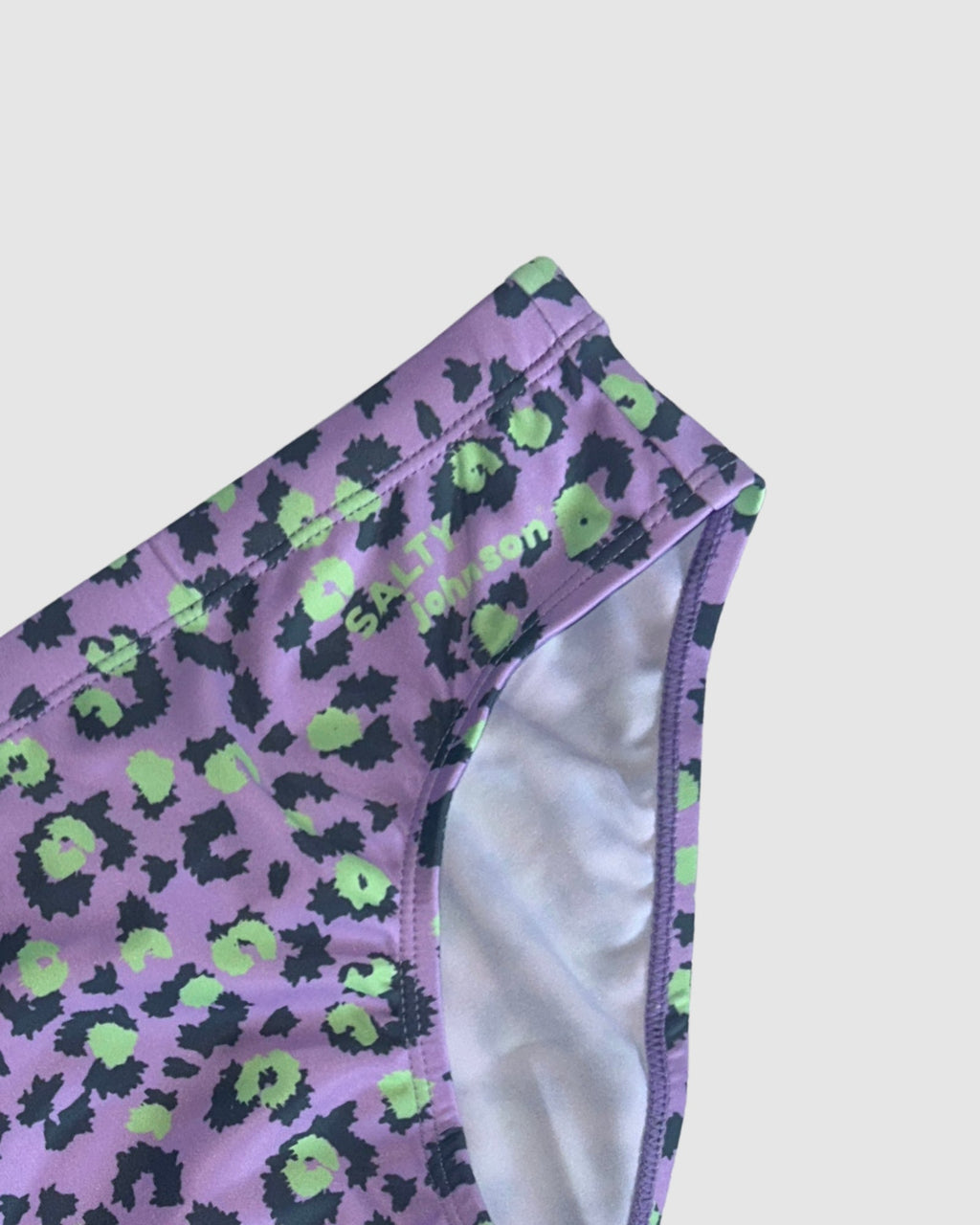 Waistband and front lining detail of Salty Johnson Purple Patch men's swim briefs in purple, black, green.