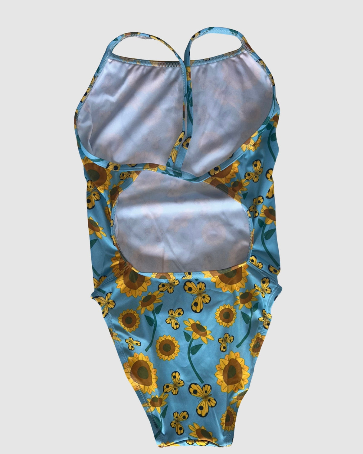 Open cross-back view of Sunny Side Up women's thin strap one-piece swimsuit, yellow sunflowers on light blue.