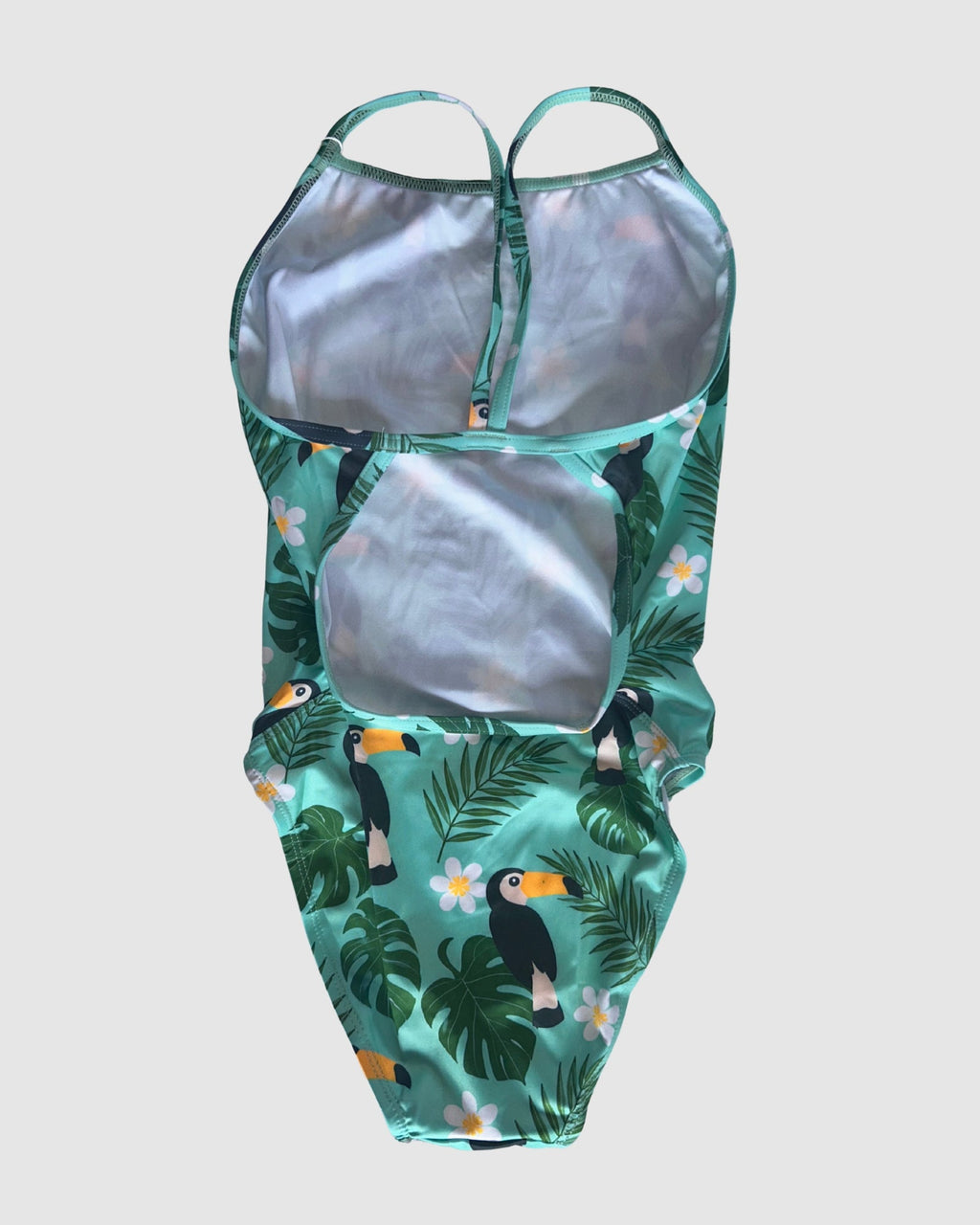 Open cross-back view of Toucan Tango women's thin strap one-piece swimsuit, toucans and tropical leaves on green.