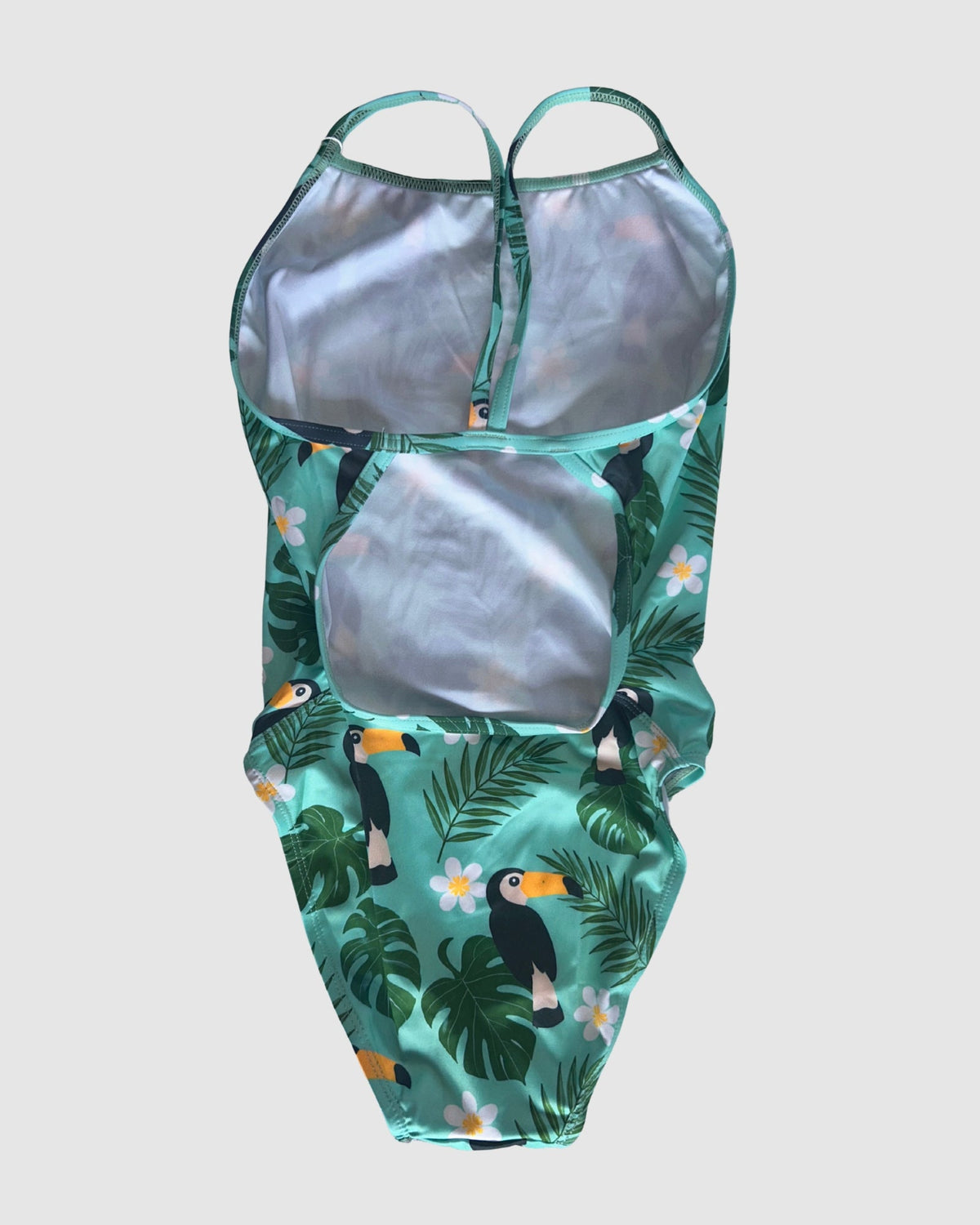 Open cross-back view of Toucan Tango women's thin strap one-piece swimsuit, toucans and tropical leaves on green.