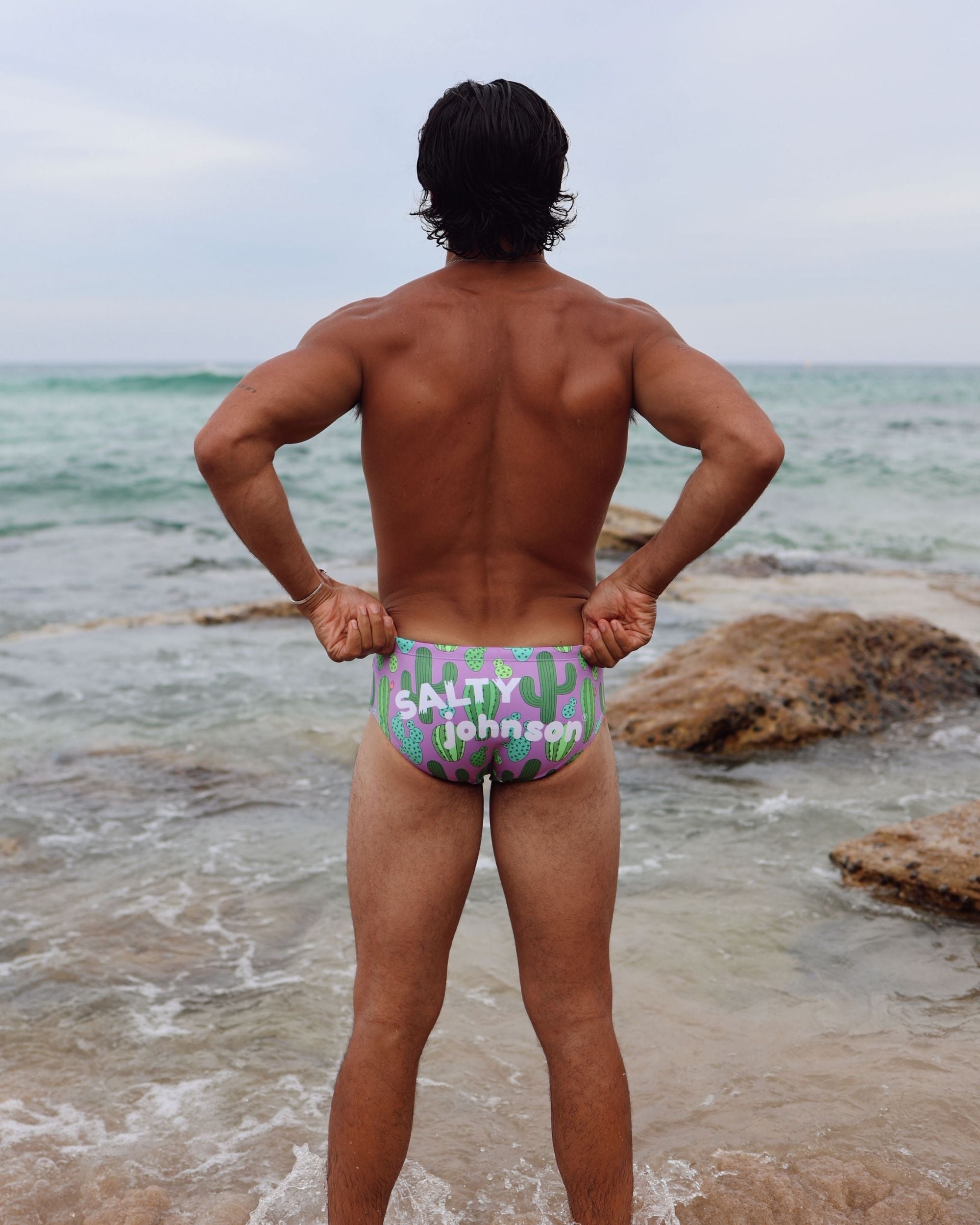 Swimmer wearing Salty Johnson flamingo-print briefs on ocean rocks