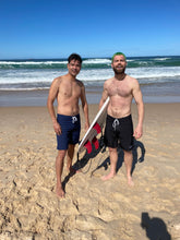 Load image into Gallery viewer, Two men wearing sustainable mens board shorts by Salty Johnson standing on a sandy beach with ocean waves in the background
