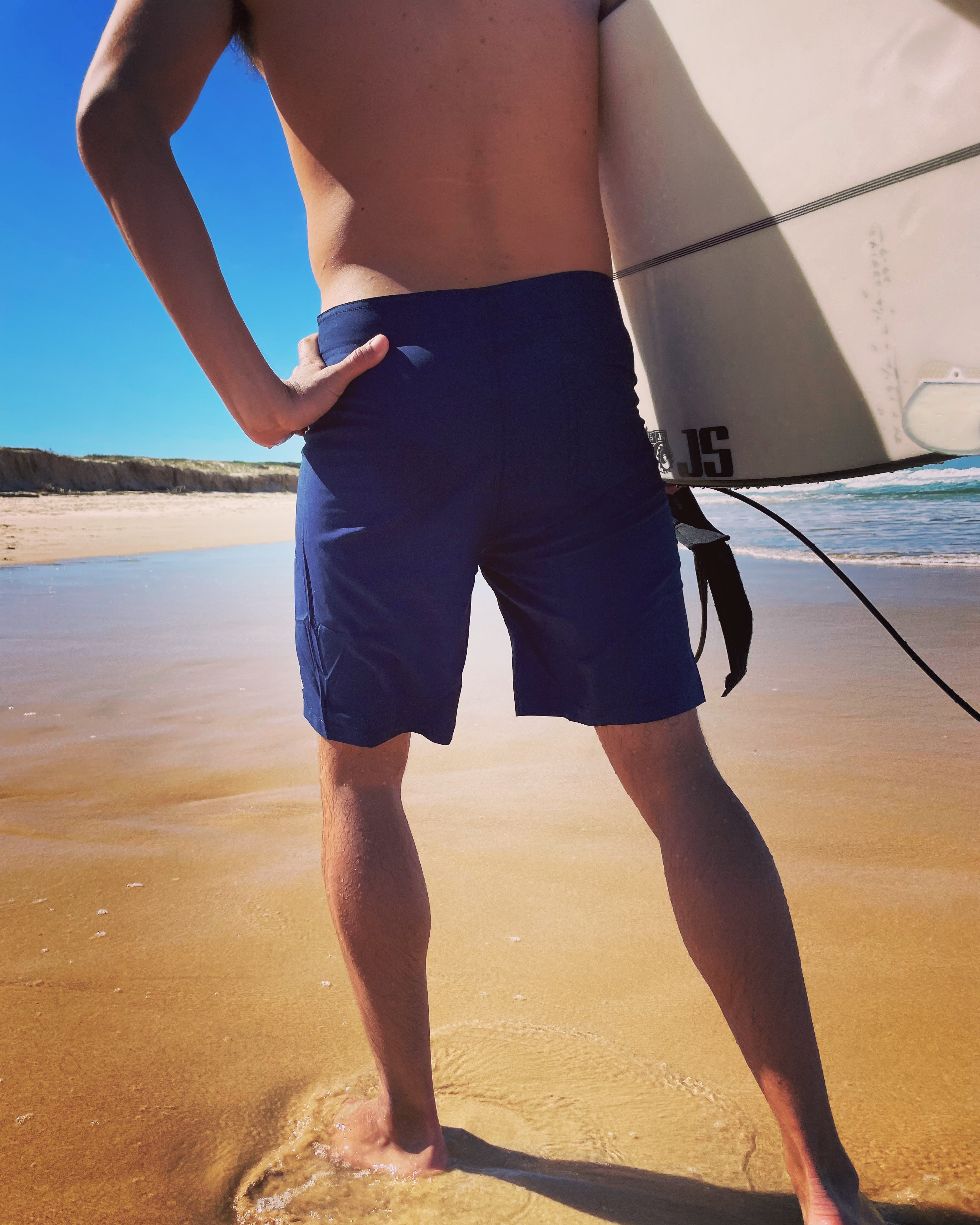 Salty Johnson sustainable mens board shorts worn by surfer standing on beach holding surfboard