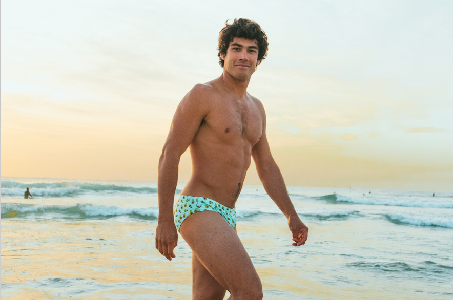 Young man wearing sustainable mens swim briefs by Salty Johnson AU walking on the beach at sunset