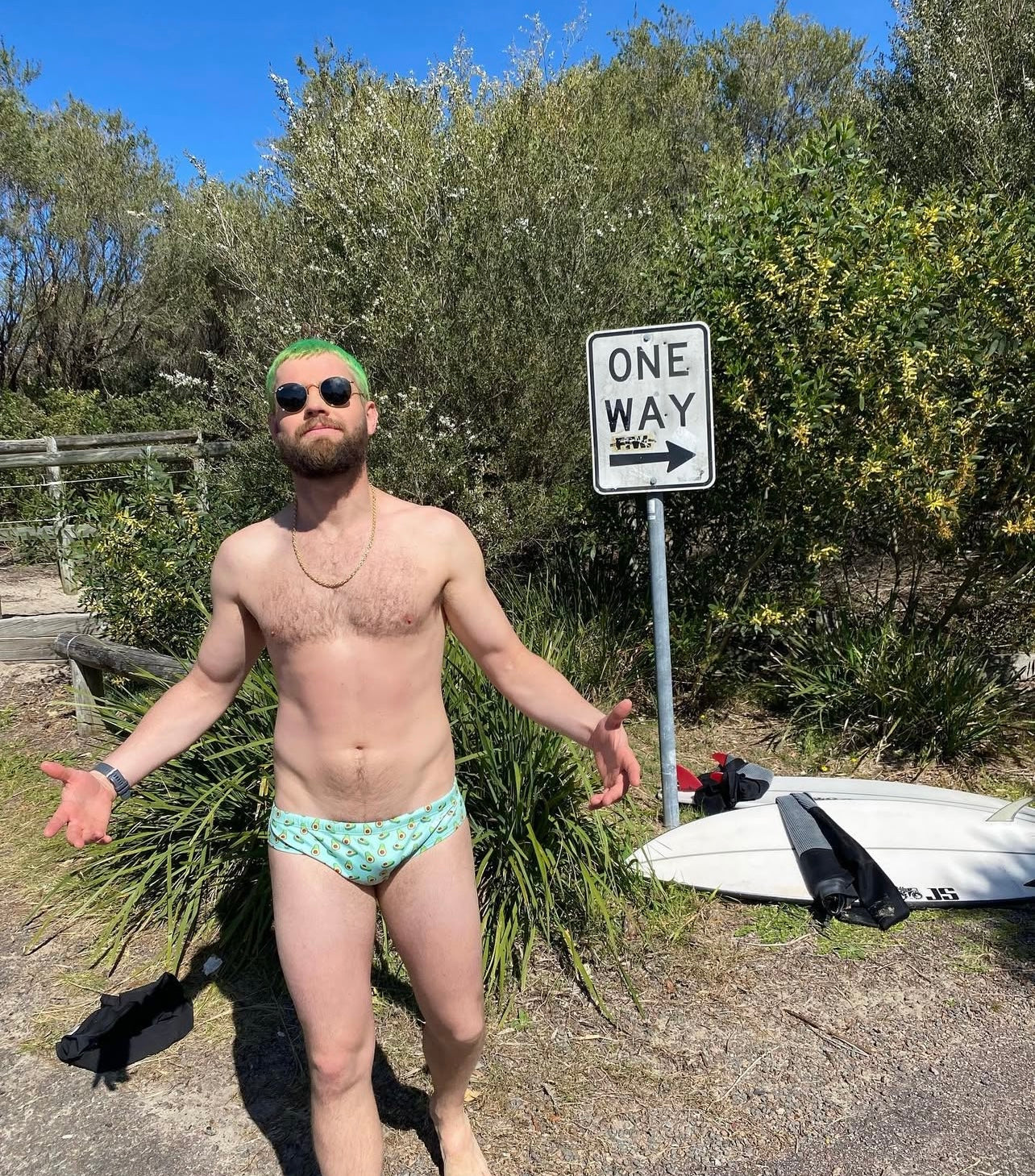 Man wearing sustainable mens swim briefs by Salty Johnson AU standing outdoors near surfboard and one way sign
