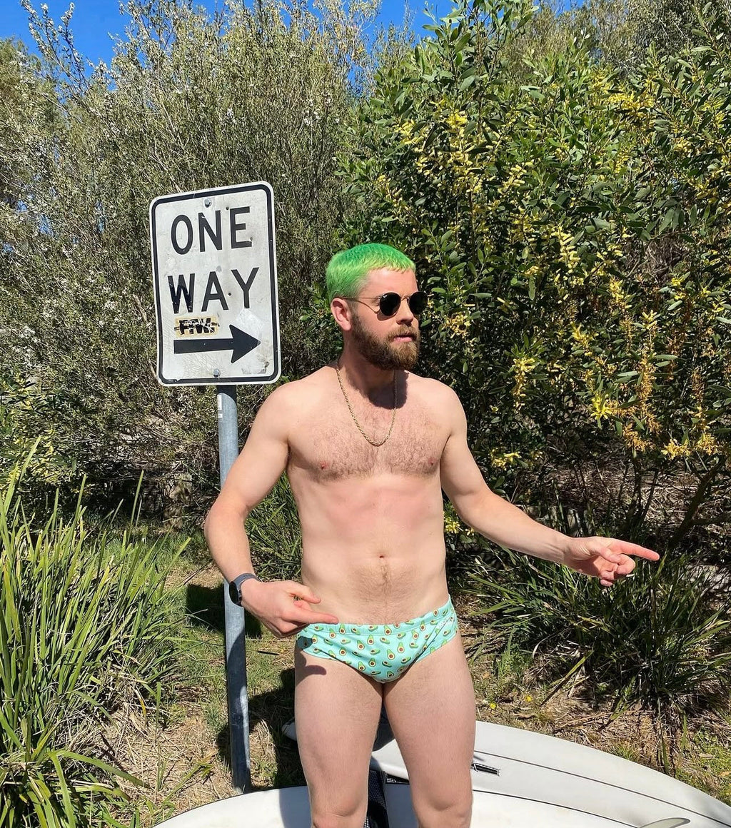 Man wearing sustainable mens swim briefs standing outdoors near a one way sign with greenery background