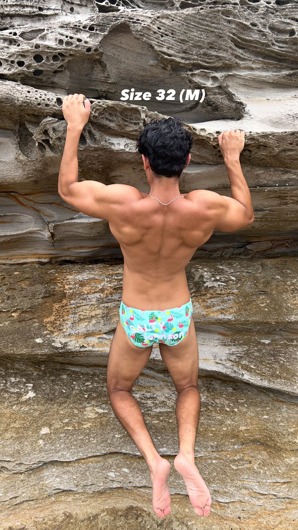 Man wearing Sustainable Mens Swim Briefs with tropical print climbing rocky cliff, size 32 medium