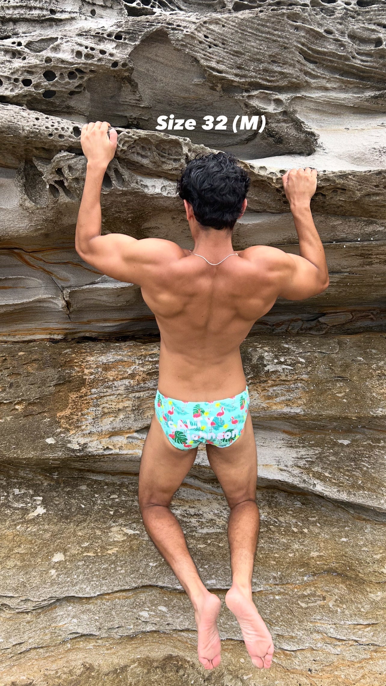 Man wearing Sustainable Mens Swim Briefs with tropical print climbing rocky cliff, size 32 medium