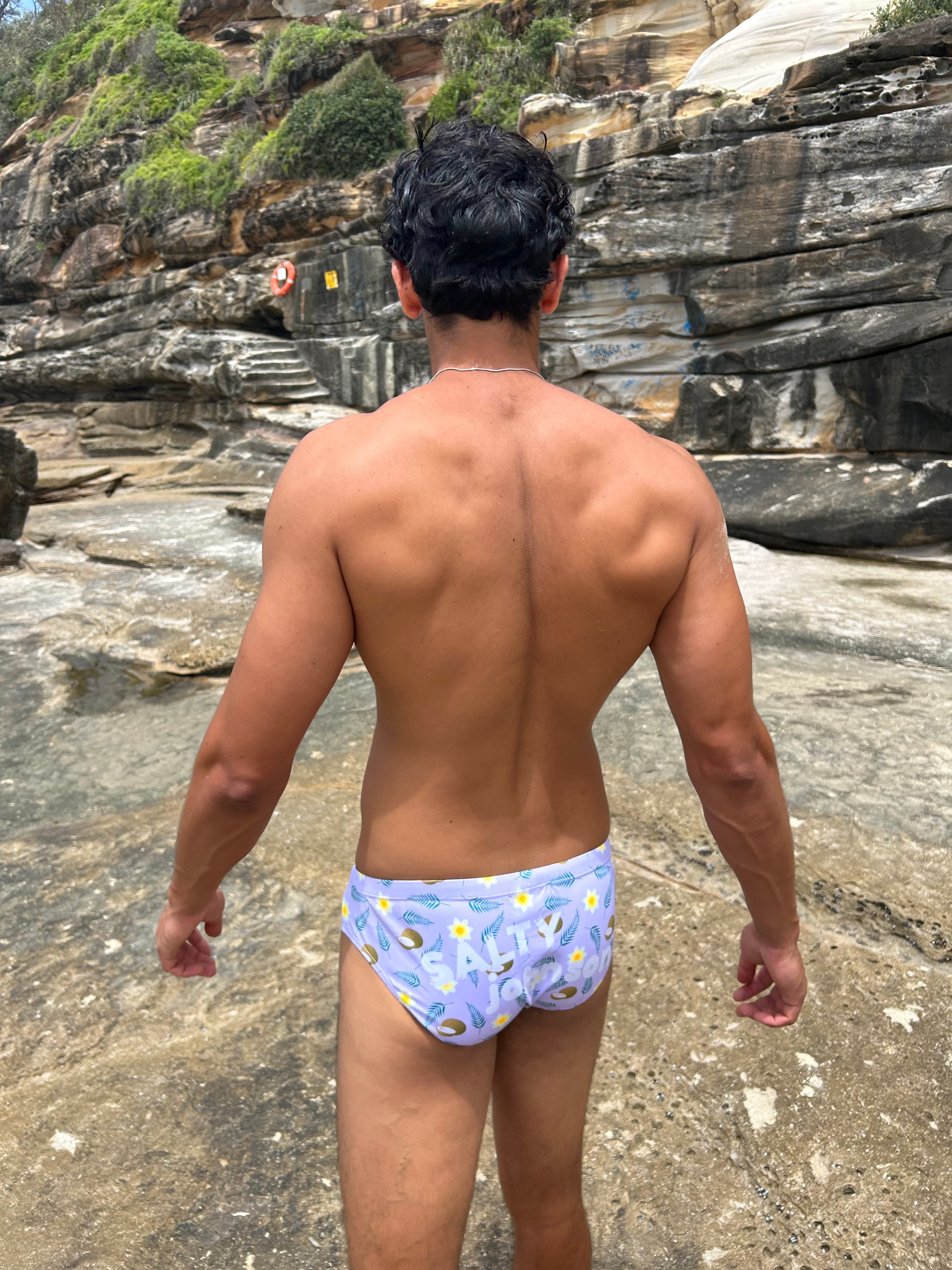 Back view of man wearing Sustainable Mens Swim Briefs by Salty Johnson AU on rocky beach background
