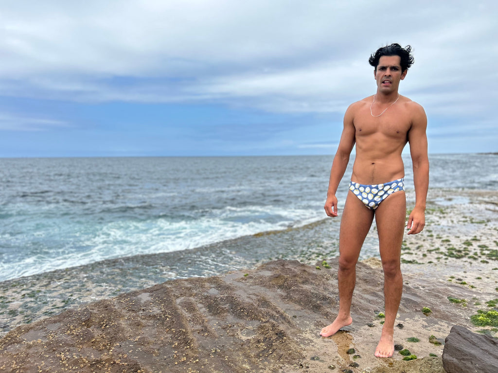 Man wearing Sustainable Mens Swim Briefs by Salty Johnson AU standing on rocky shore by the ocean