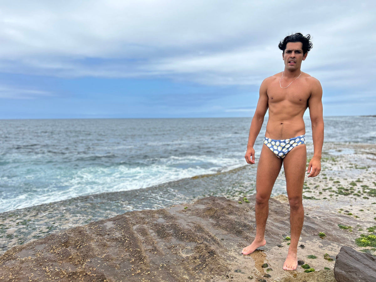 Man wearing Sustainable Mens Swim Briefs by Salty Johnson AU standing on rocky shore by the ocean