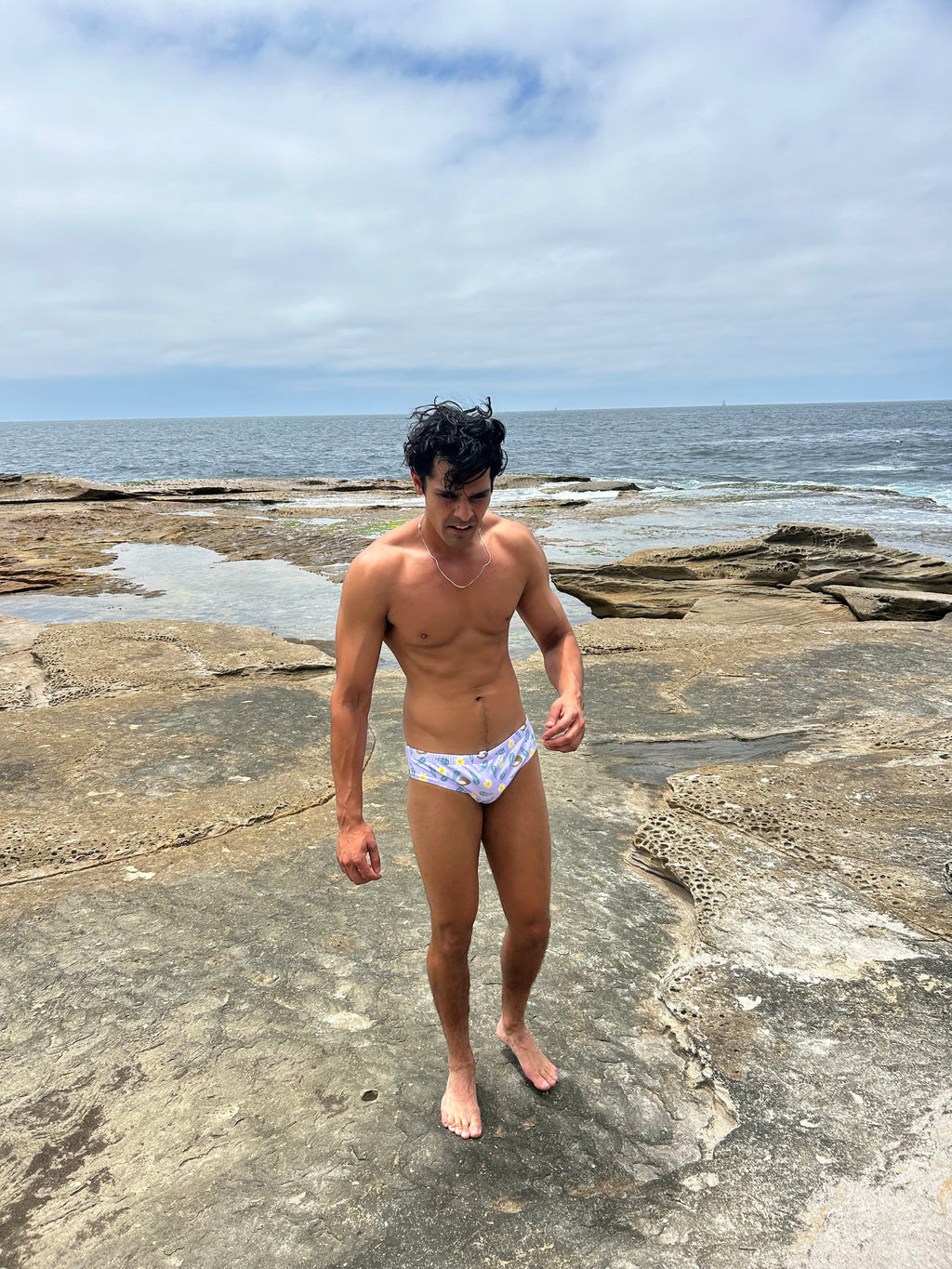 Man wearing Sustainable Mens Swim Briefs on rocky beach by ocean from Salty Johnson AU