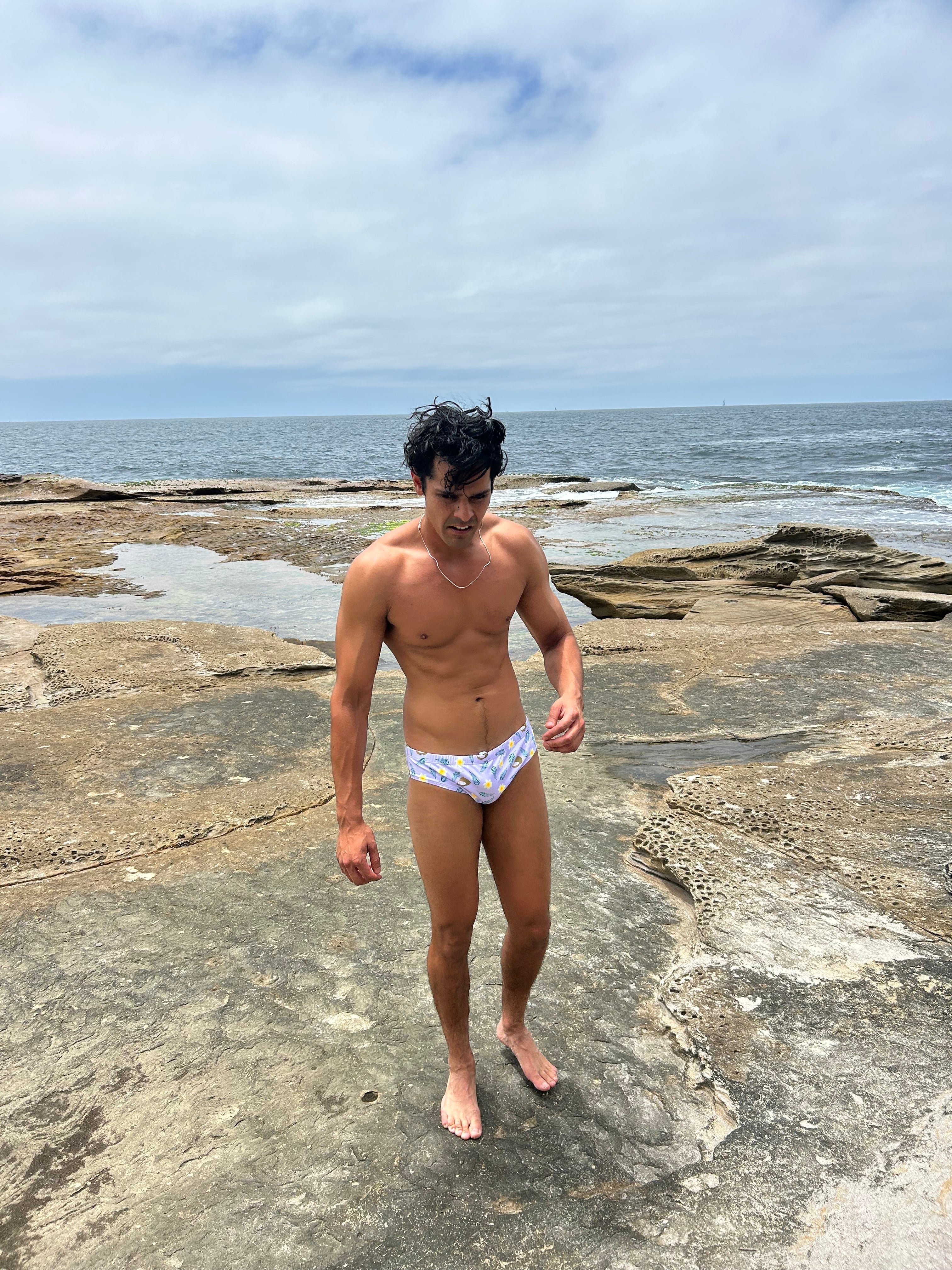 Man wearing Sustainable Mens Swim Briefs on rocky beach by ocean from Salty Johnson AU