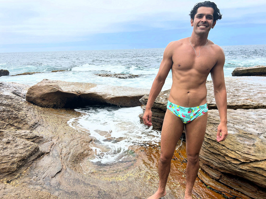 Man wearing Salty Johnson AU sustainable mens swim briefs with tropical print by the ocean rocks