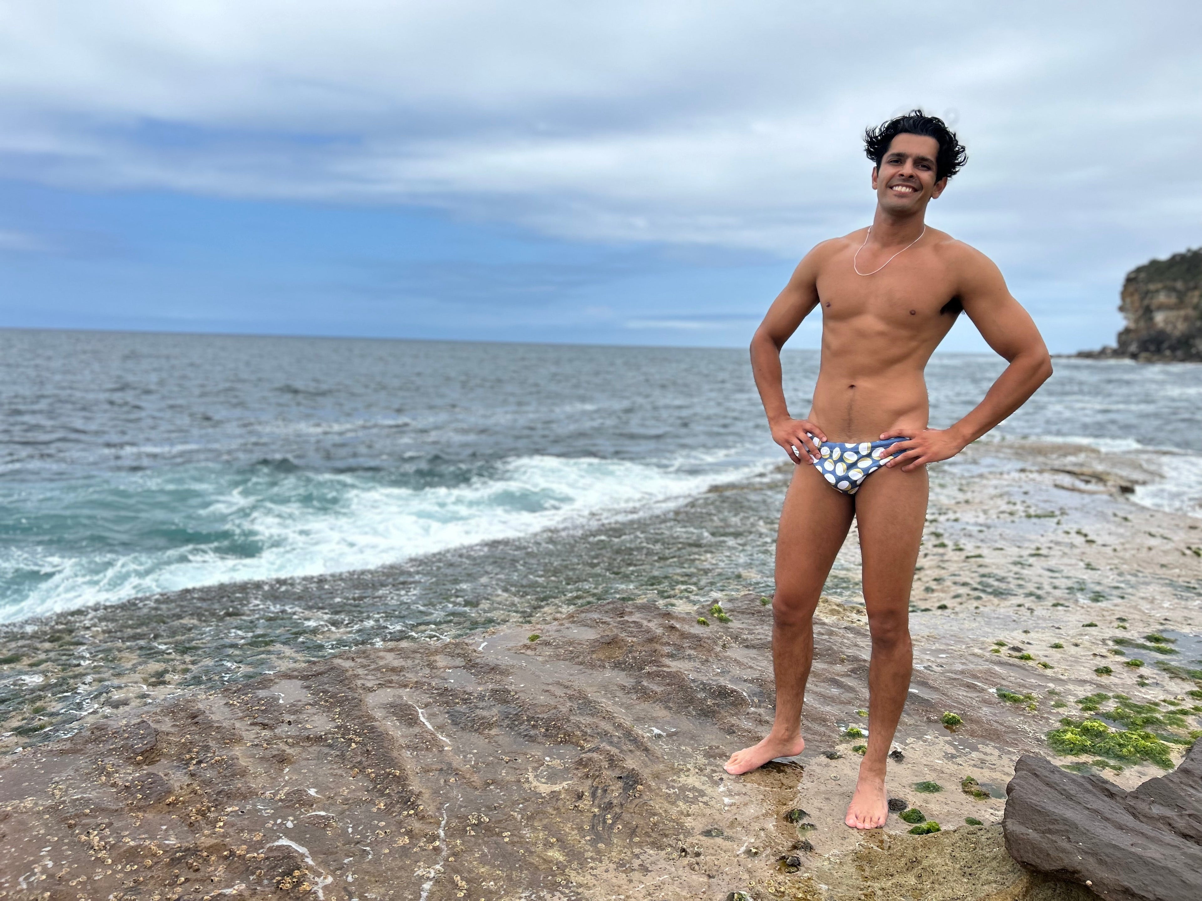 Man wearing Sustainable Mens Swim Briefs by Salty Johnson AU standing on rocky beach near ocean