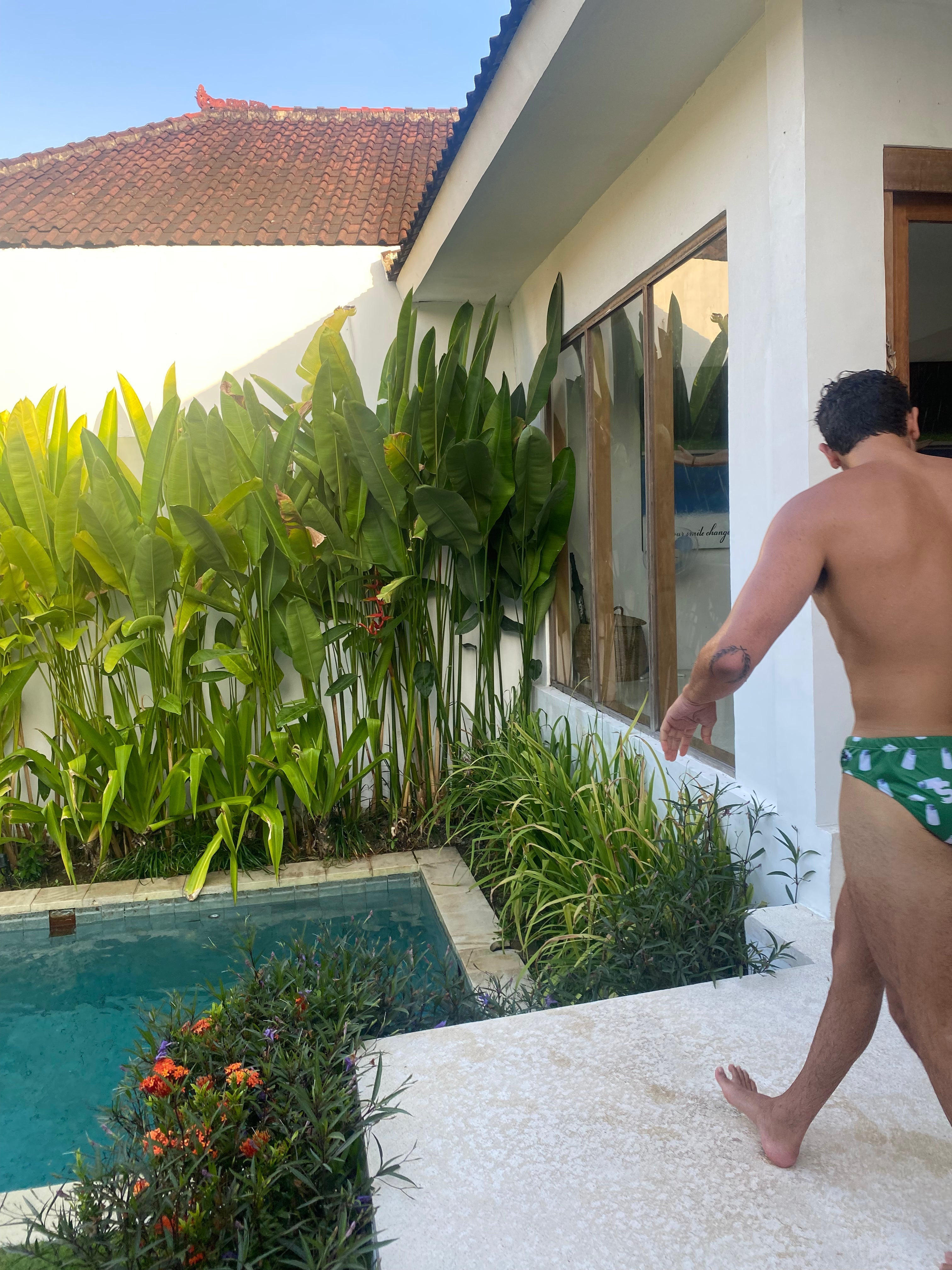 Man wearing Salty Johnson sustainable mens swim briefs with green tropical print near poolside in sunny backyard