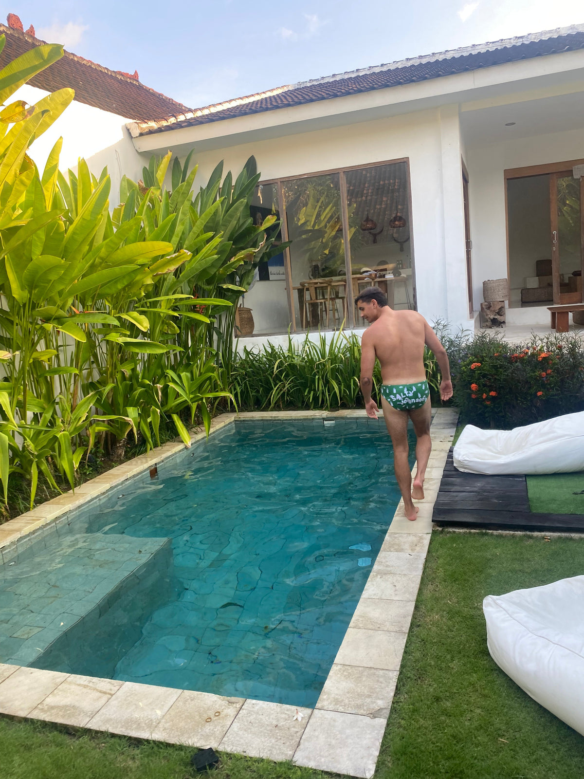 Man wearing sustainable mens swim briefs by Salty Johnson walking by a private pool with tropical plants