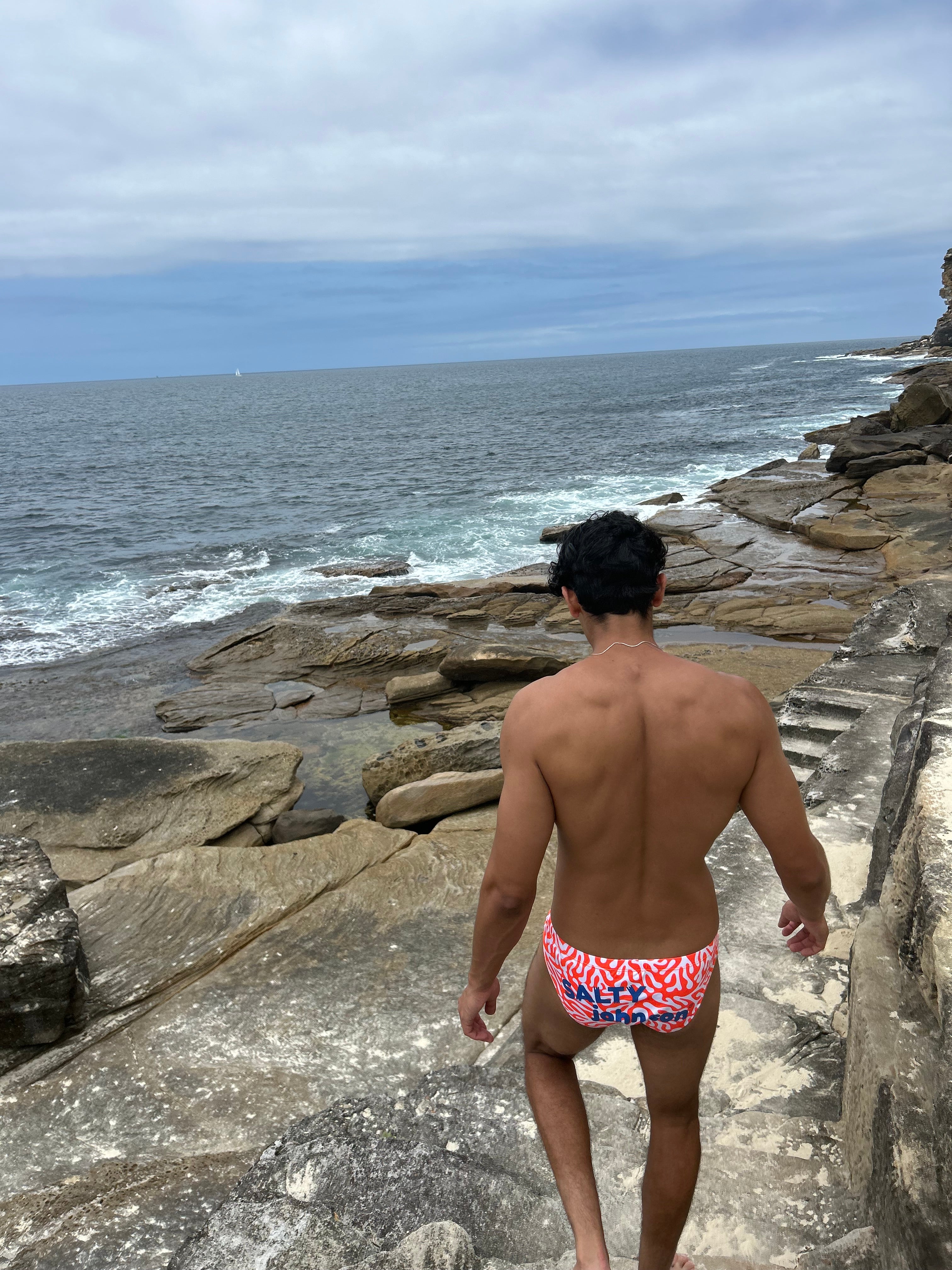 Man wearing Sustainable Mens Swim Briefs by Salty Johnson AU walking on rocky coastline