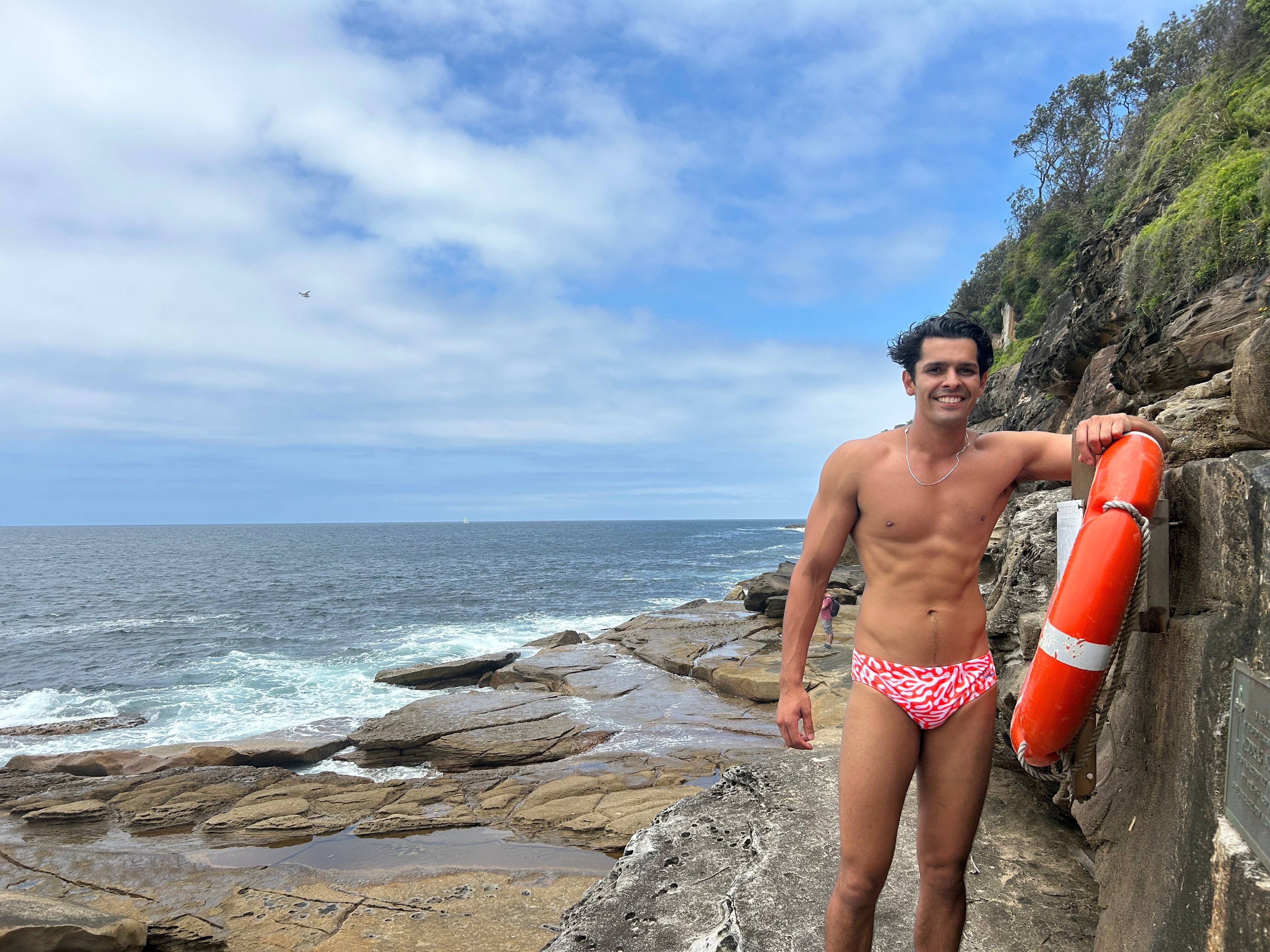 Man wearing Salty Johnson AU sustainable mens swim briefs standing on rocky ocean shore holding a lifebuoy